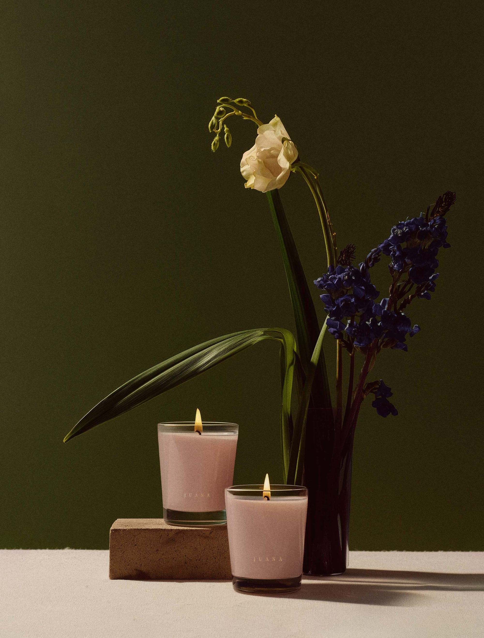 Two Juana Rose+Jasmine Romance Arouse apothecary candles next to flower in vase, vegan, eco-friendly.