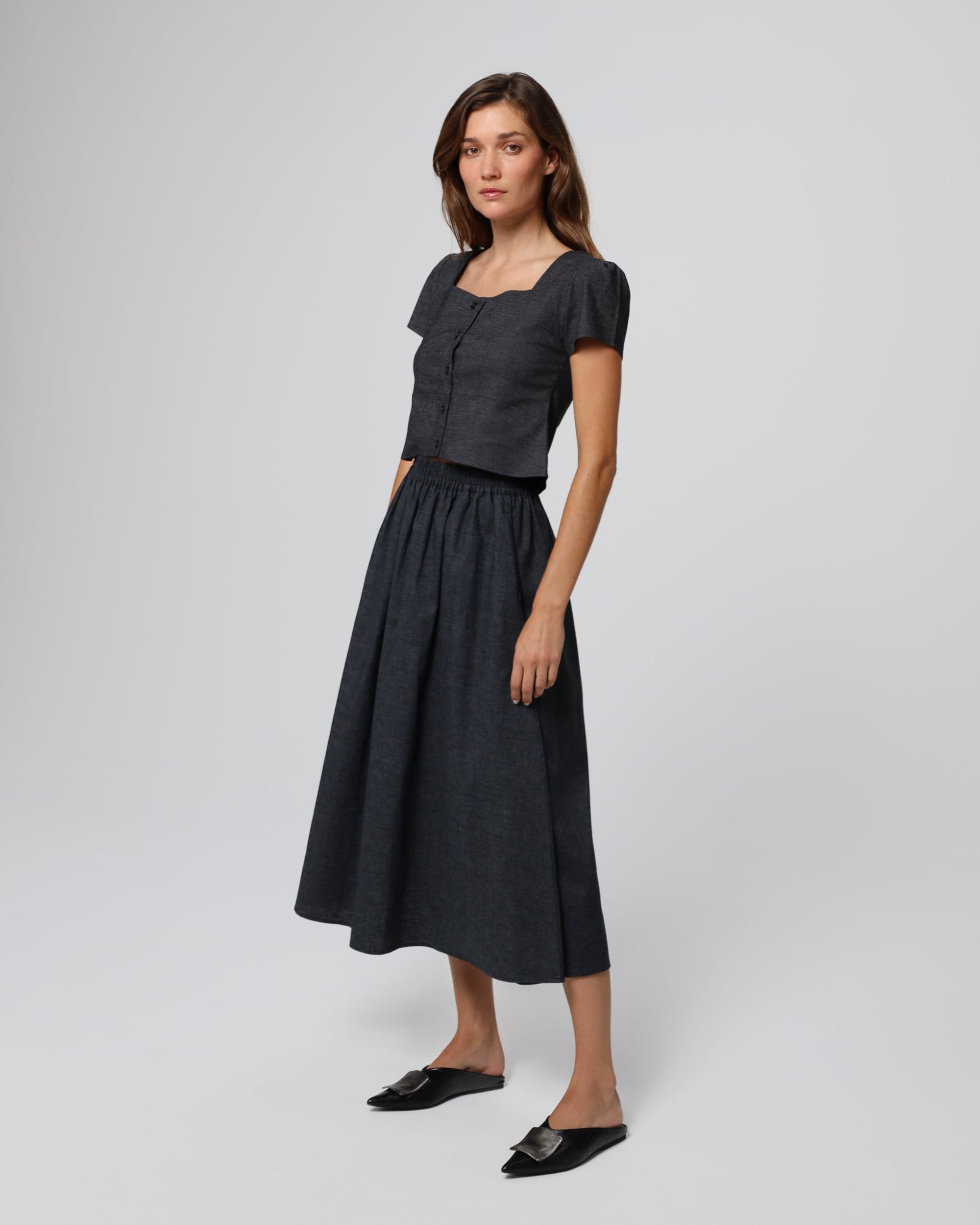 Model wearing Juana Hemp Blend Maxi Skirt in black hemp blend twill, showing soft pleats and flowing silhouette.