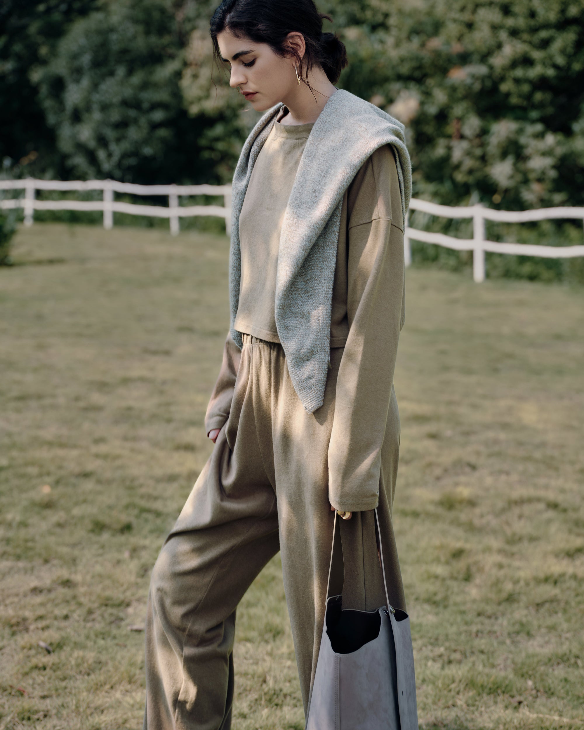 Side profile along a white-fence path showing Aera set olive; cropped boxy top and easy wide-leg drape.