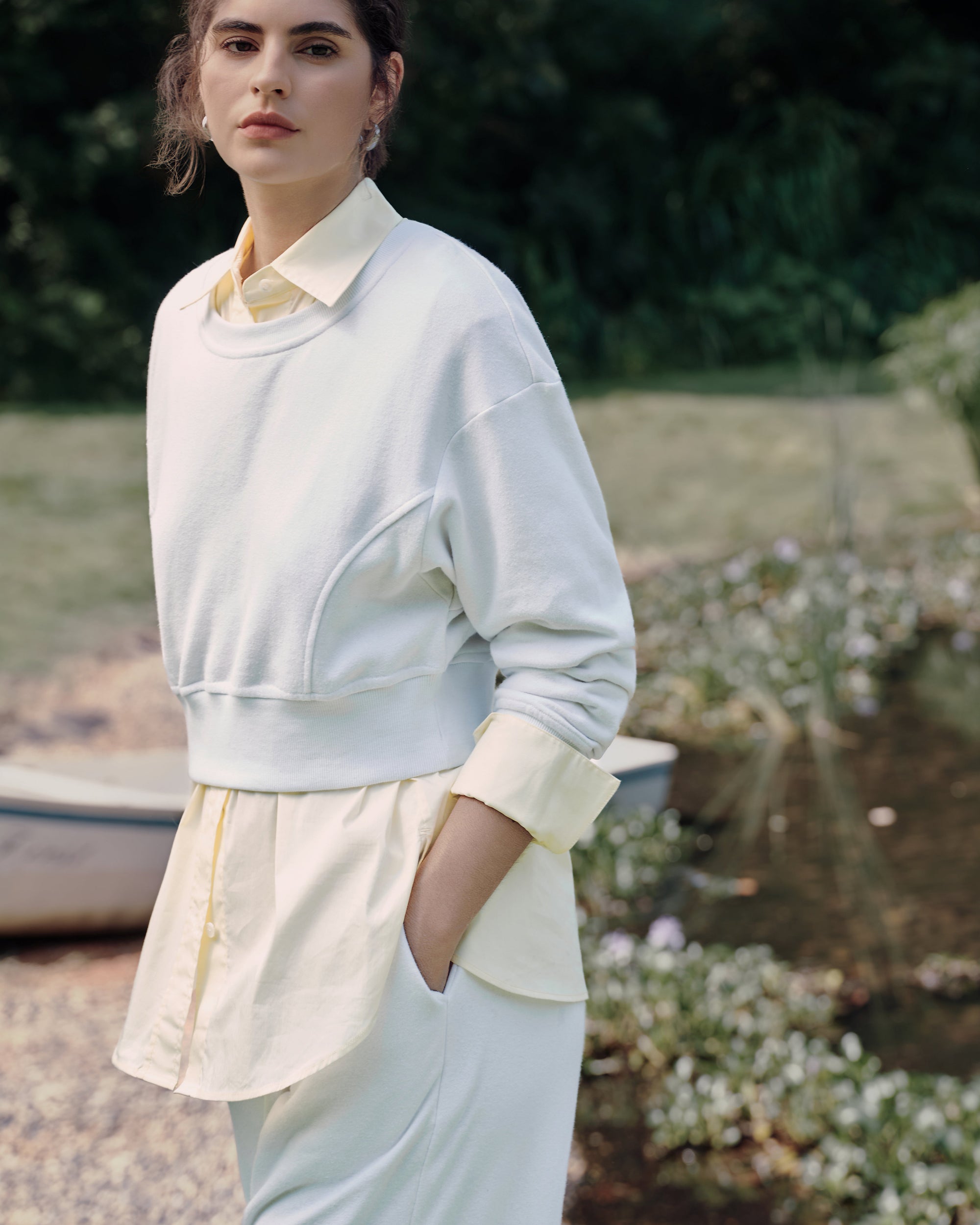 Garden standing shot of the white fleece set (hemp–organic cotton) with long light-yellow shirt peeking beneath the cropped hem; minimal, relaxed silhouette.