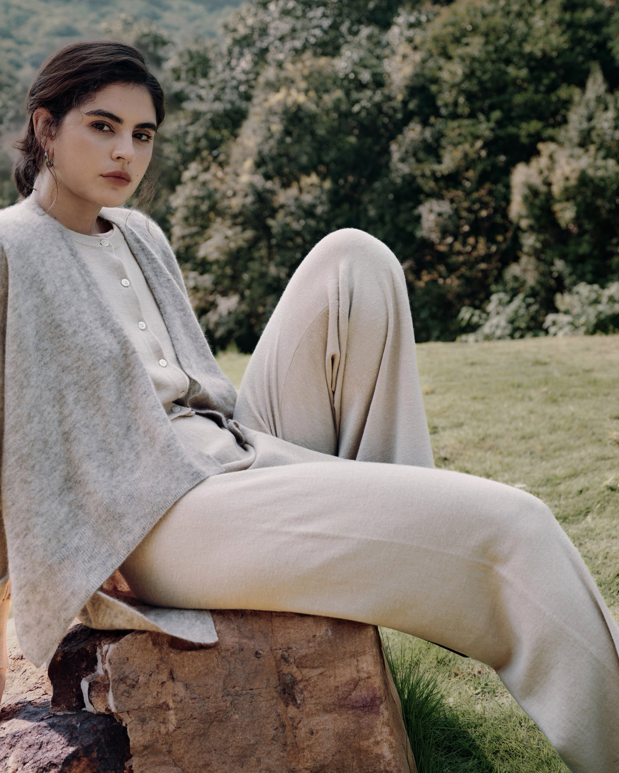 Garden seated portrait wearing Cashmere Cape oatmeal over Liora beige and Nilo beige, highlighting relaxed, elegant layering.