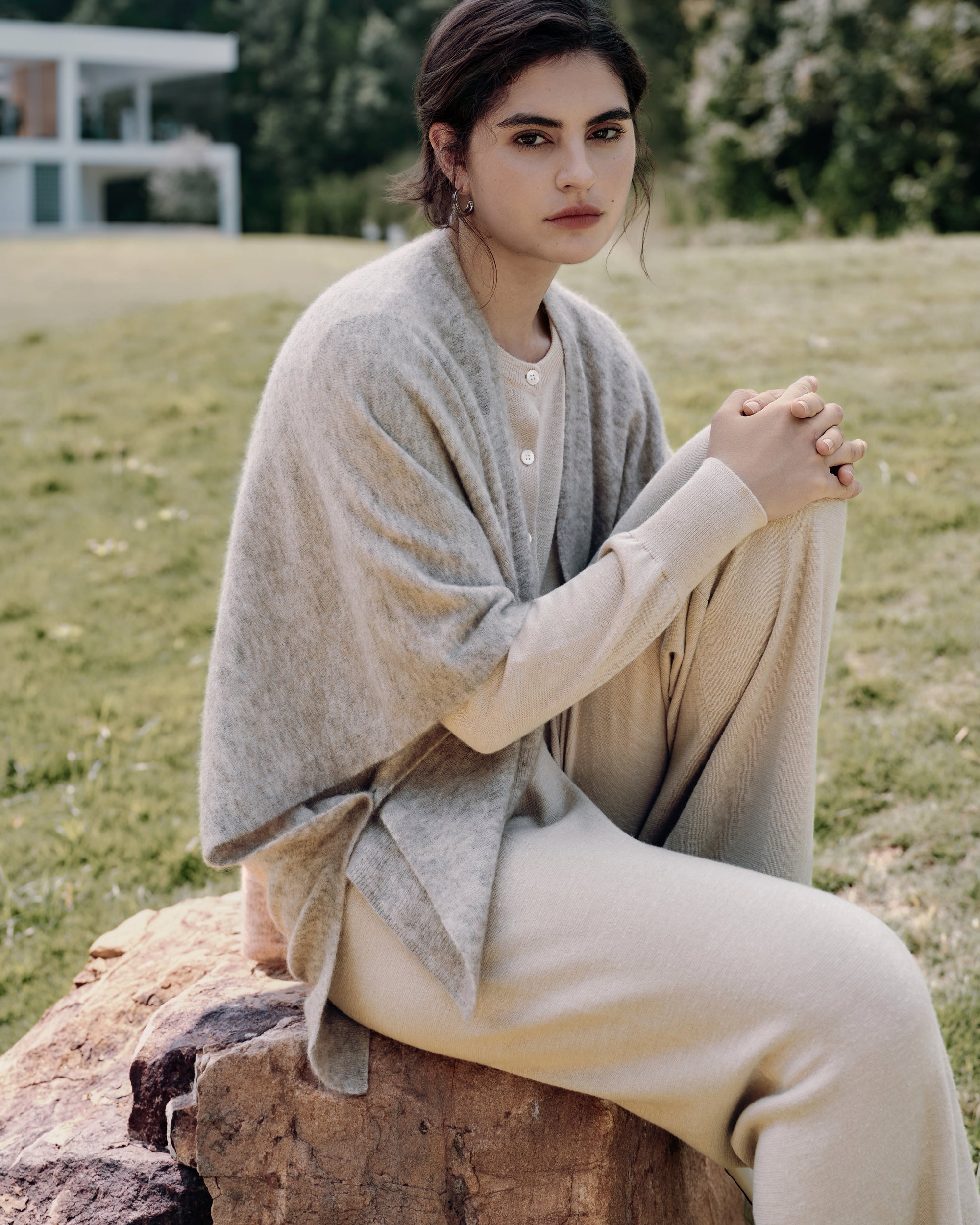 Side-profile on garden path showing cape edge (oatmeal), cardigan line (beige), and pants drape (beige).