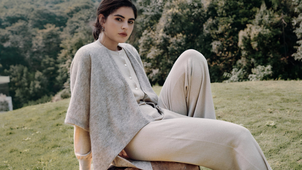 Garden seated portrait wearing Cashmere Cape oatmeal over Liora beige and Nilo beige, highlighting relaxed, elegant layering.