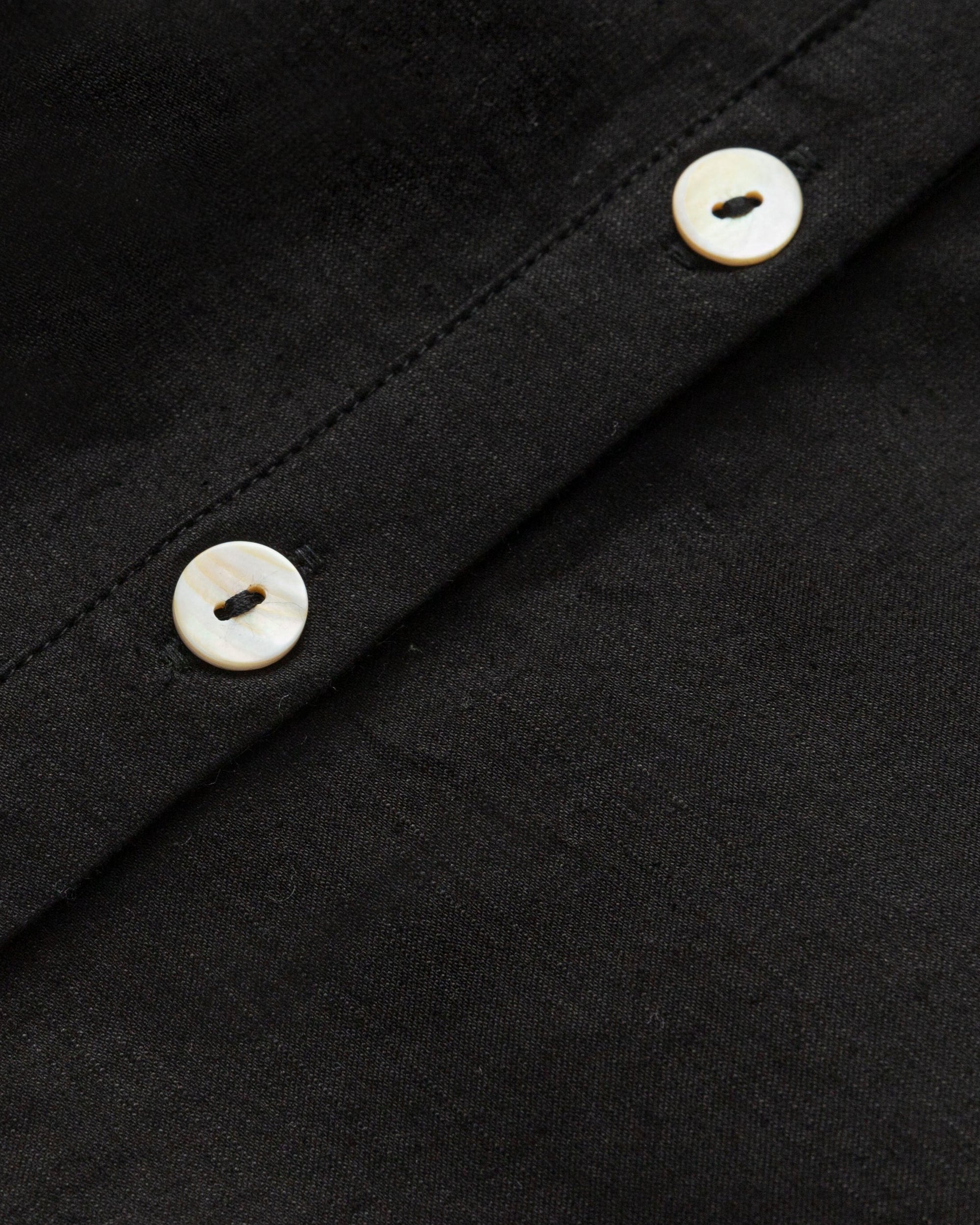 Detail shot of natural shell buttons and stitching on the Aella Long Sleeve Woven Top (black).