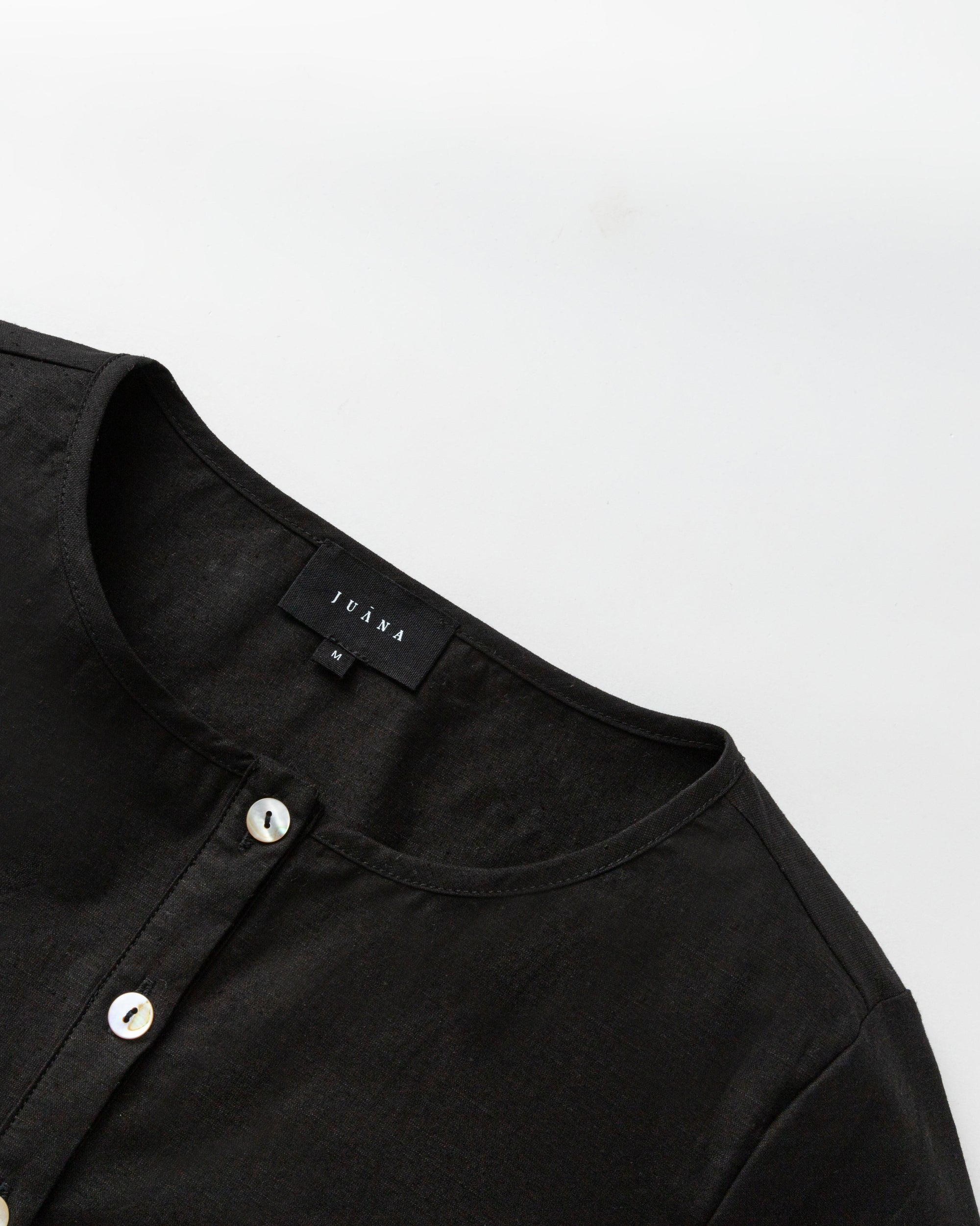 Flat lay of Aella Long Sleeve Woven Top (black), showing structure and precise finishing.