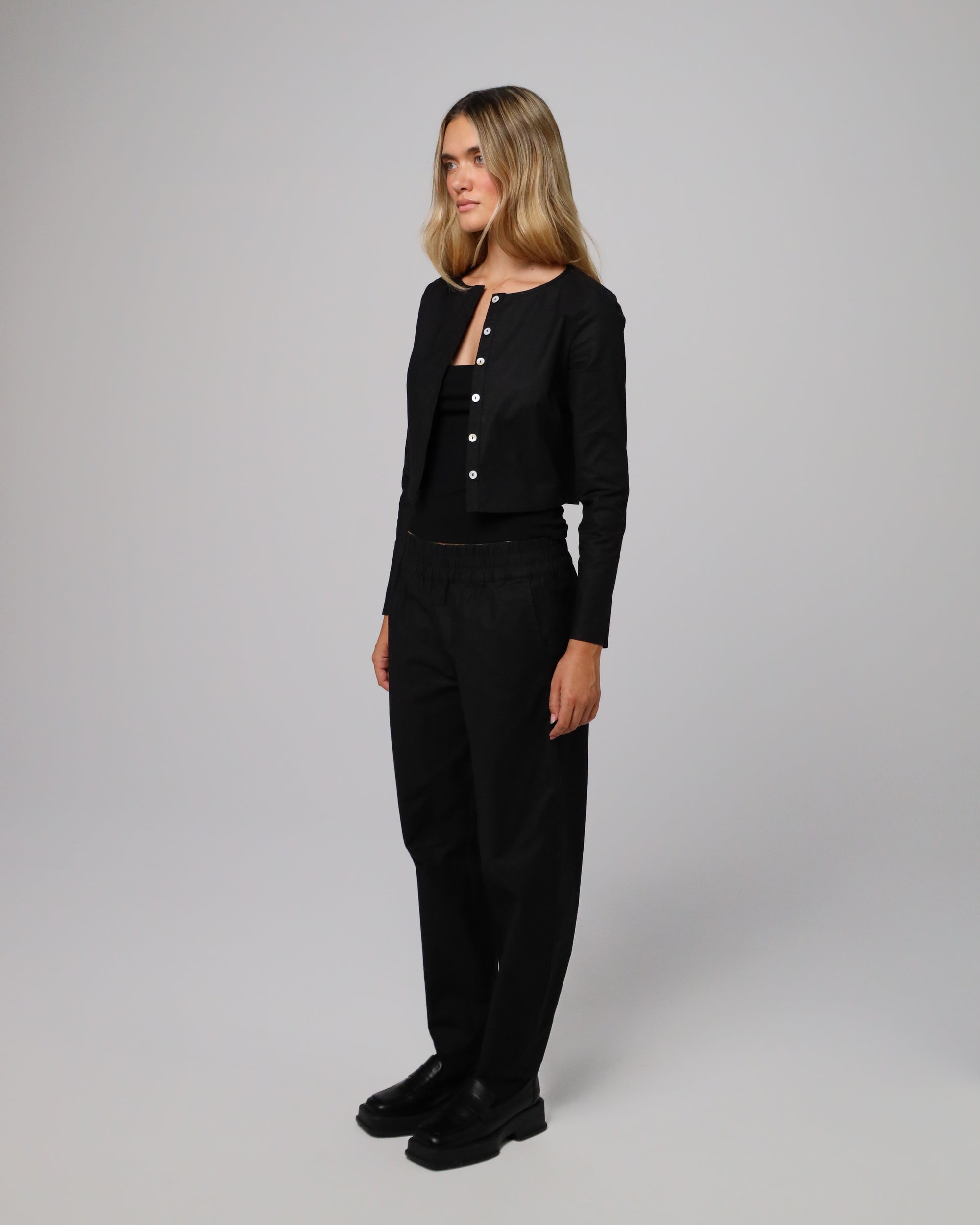 Side view of Aella Long Sleeve Woven Top (black) paired with Aella Mid Rise Relaxed Pants for a matching set.