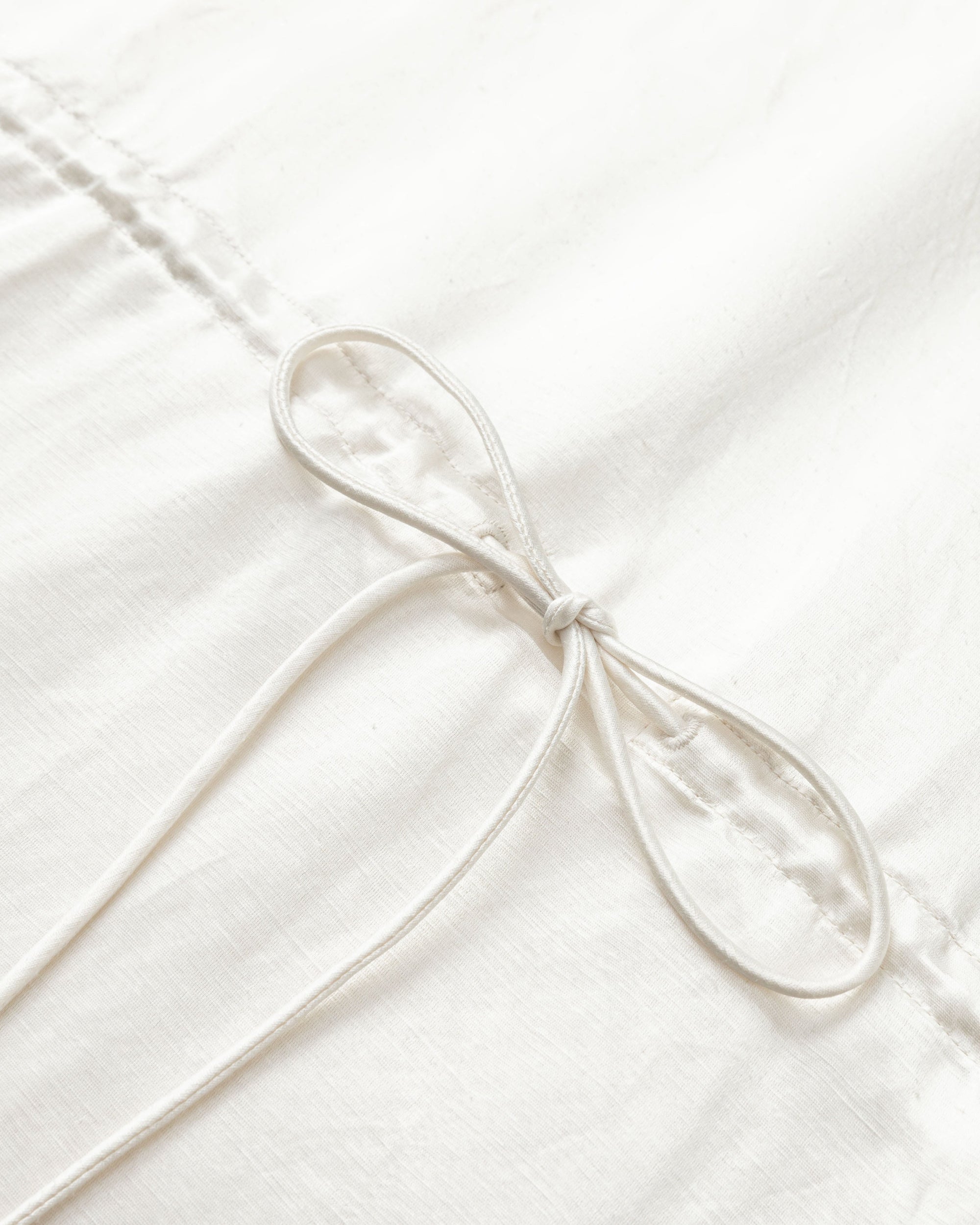 Flat lay of Aven Raglan Dress (pearl white), showing hemp–silk fabric sheen and minimalist detailing.