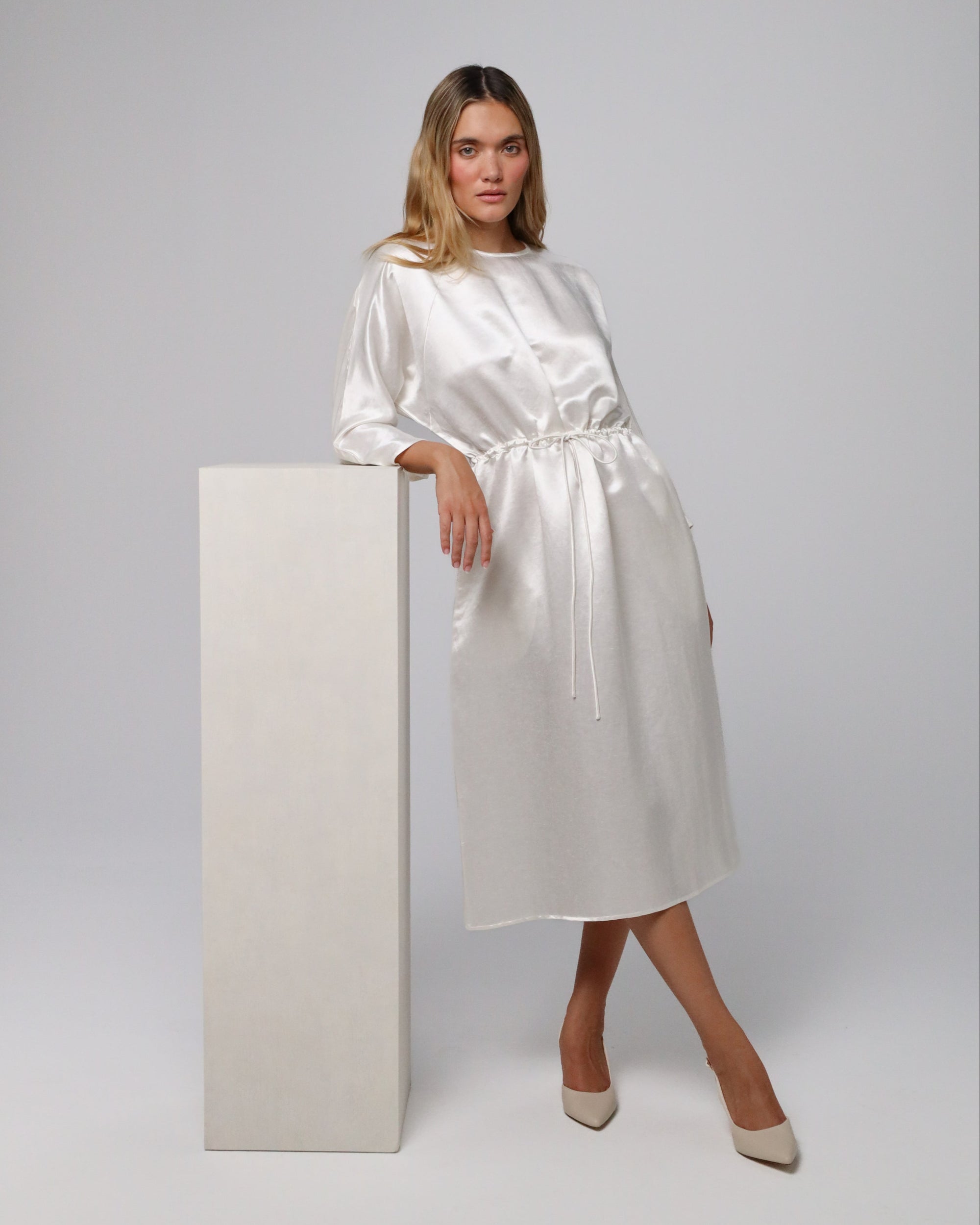 Model presenting Aven Raglan Dress (pearl white) in an evening look, accessorized for formal wear.