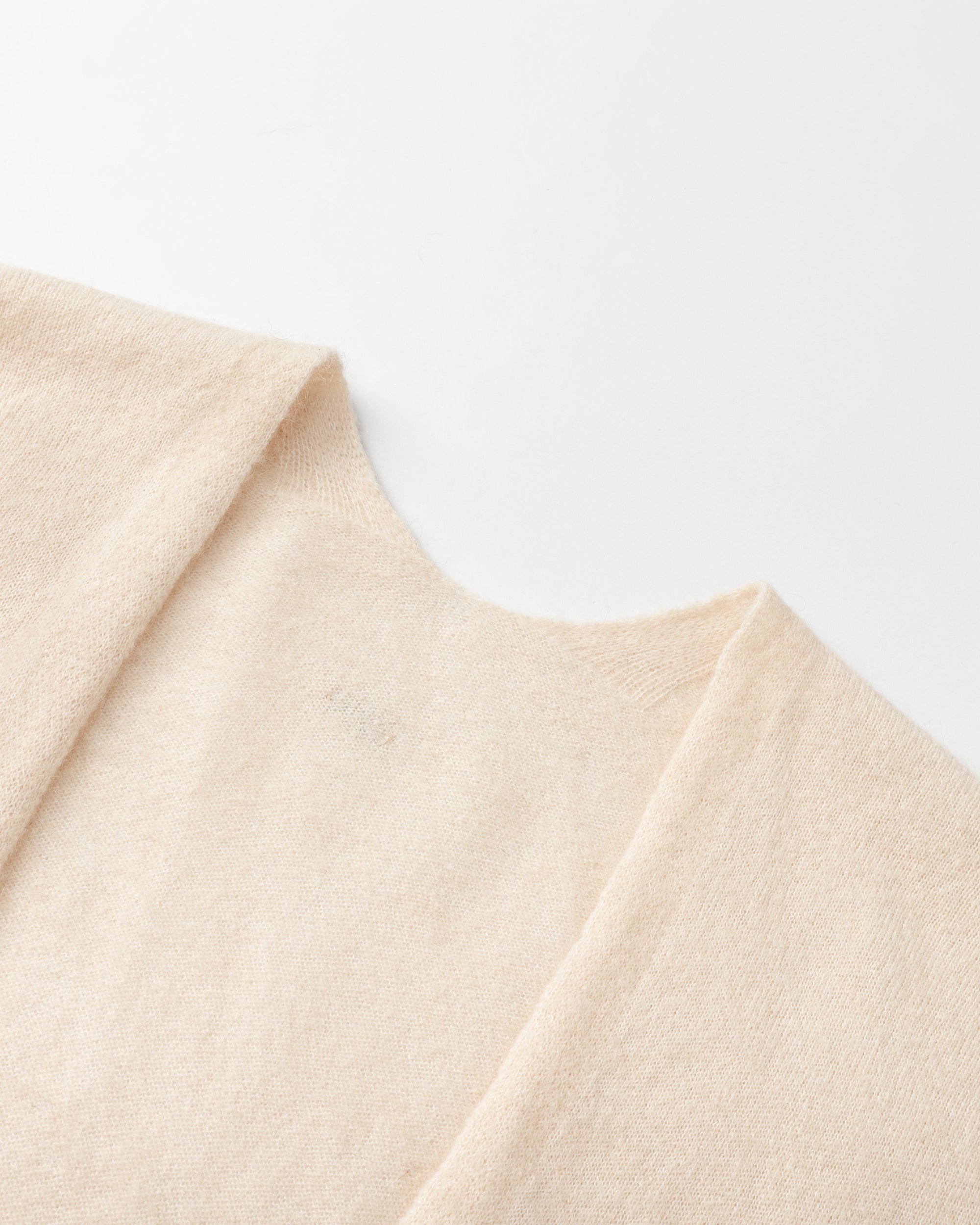 Detail of neckline and edge finish on almond milk wool–cashmere–hemp cape; refined trim and drape.