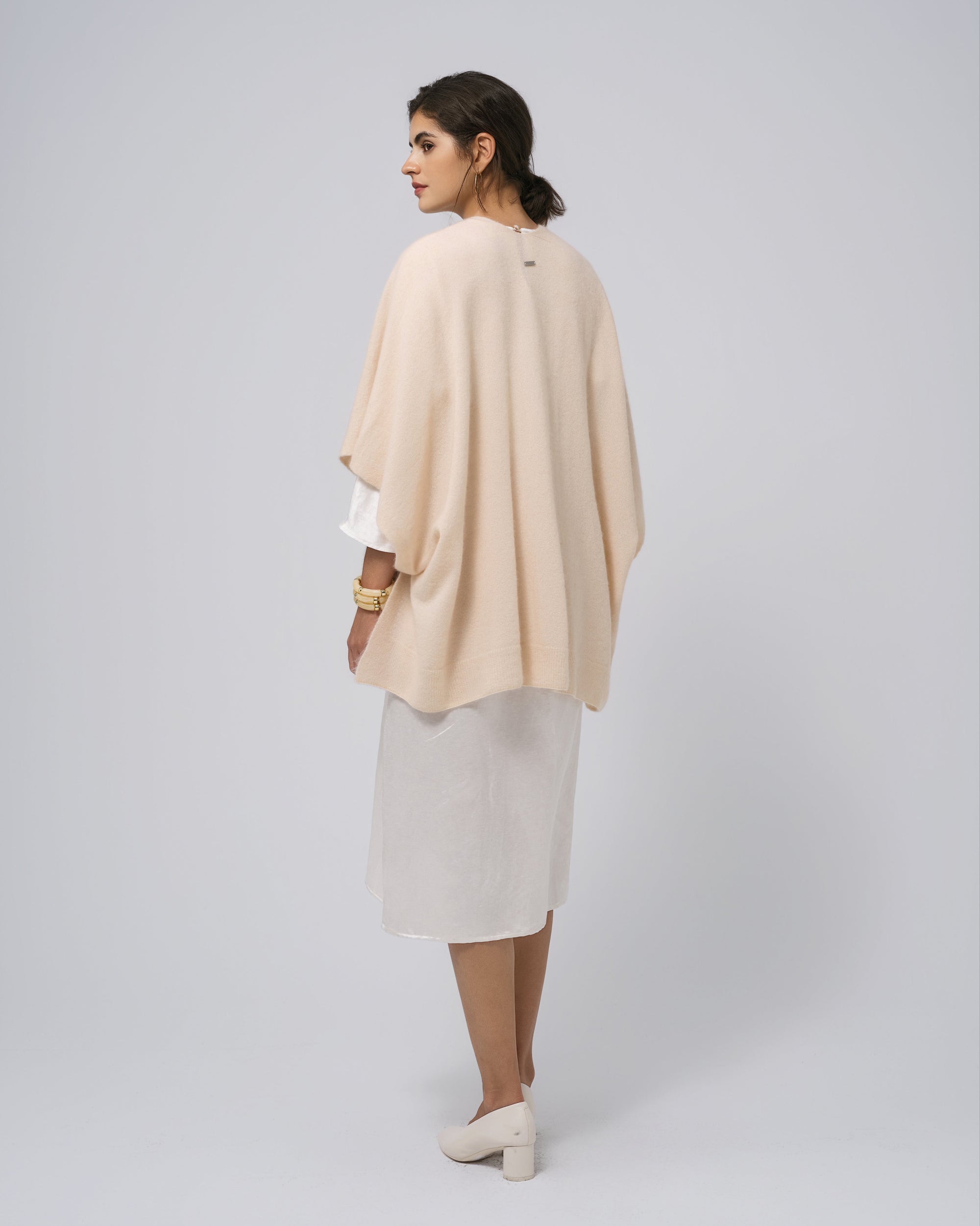 Model back view of almond milk cape; smooth back panel and flowing hem.