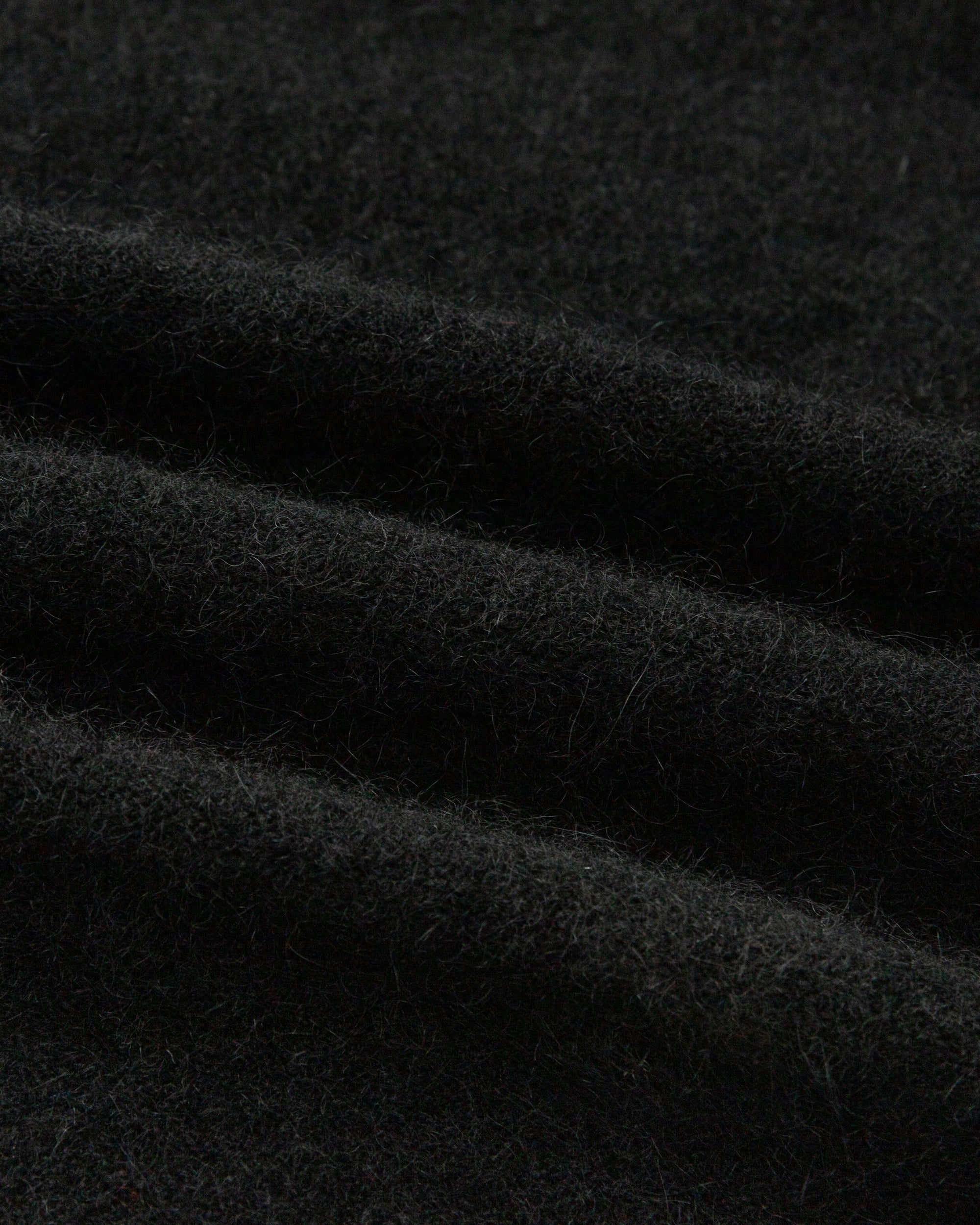 Textile close-up of black wool–cashmere–hemp knit; soft handfeel and fine gauge.