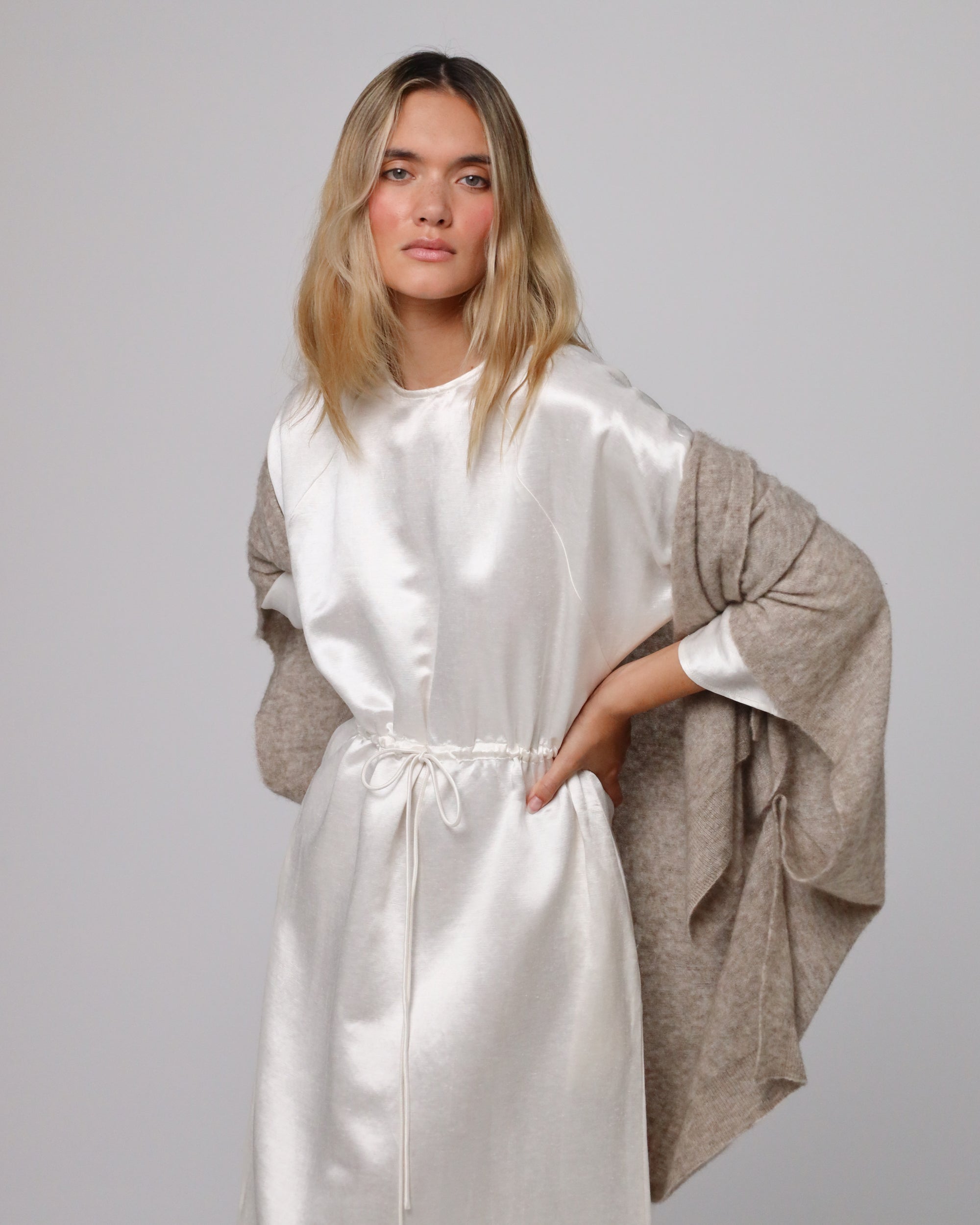 Model styling Juana Cashmere Cape (oatmeal) over a knit dress, highlighting lightweight warmth and elegant flow.