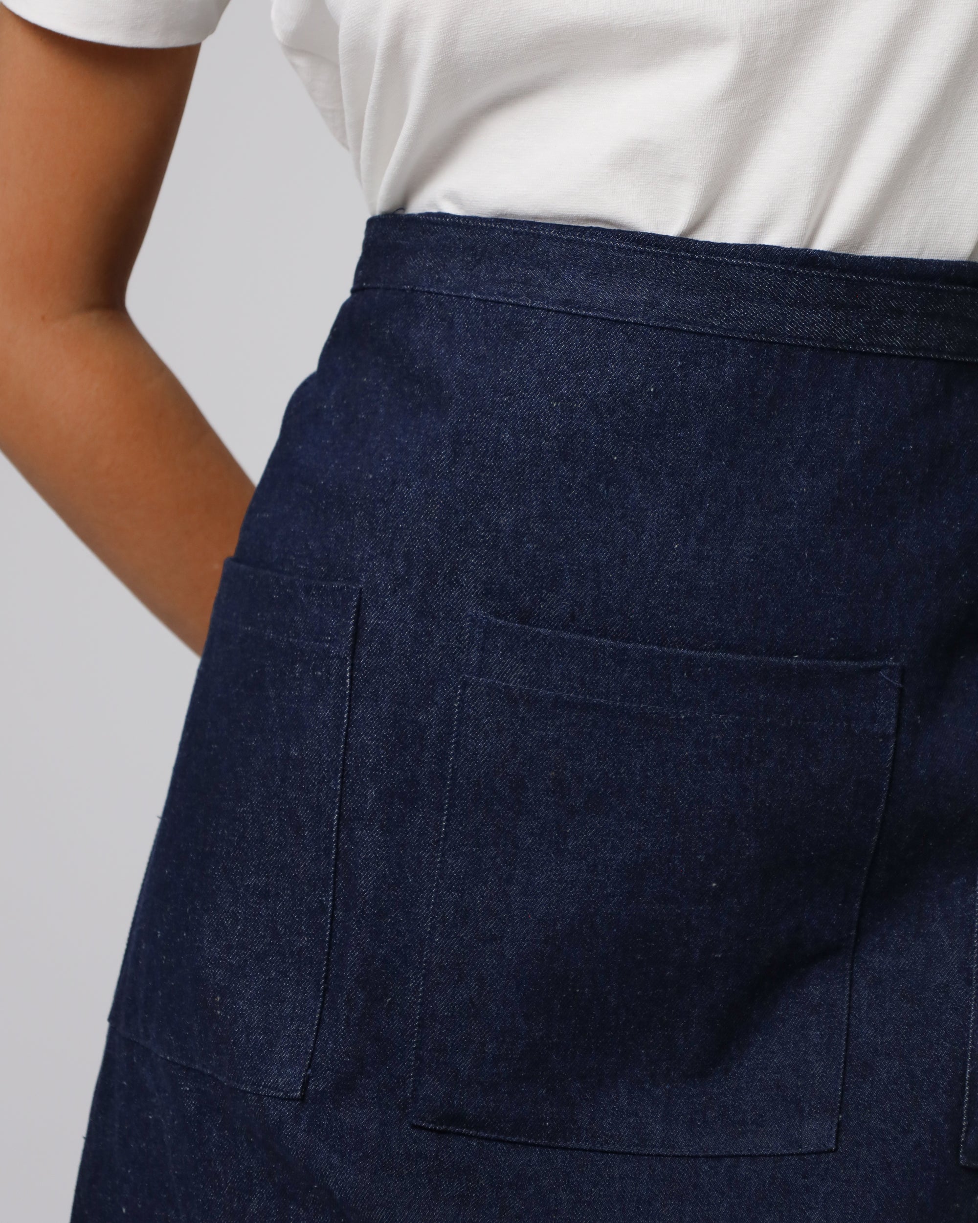 Detail shot of adjustable buttoned straps and reinforced pocket stitching on Denim Atelier Functional Apron (indigo).