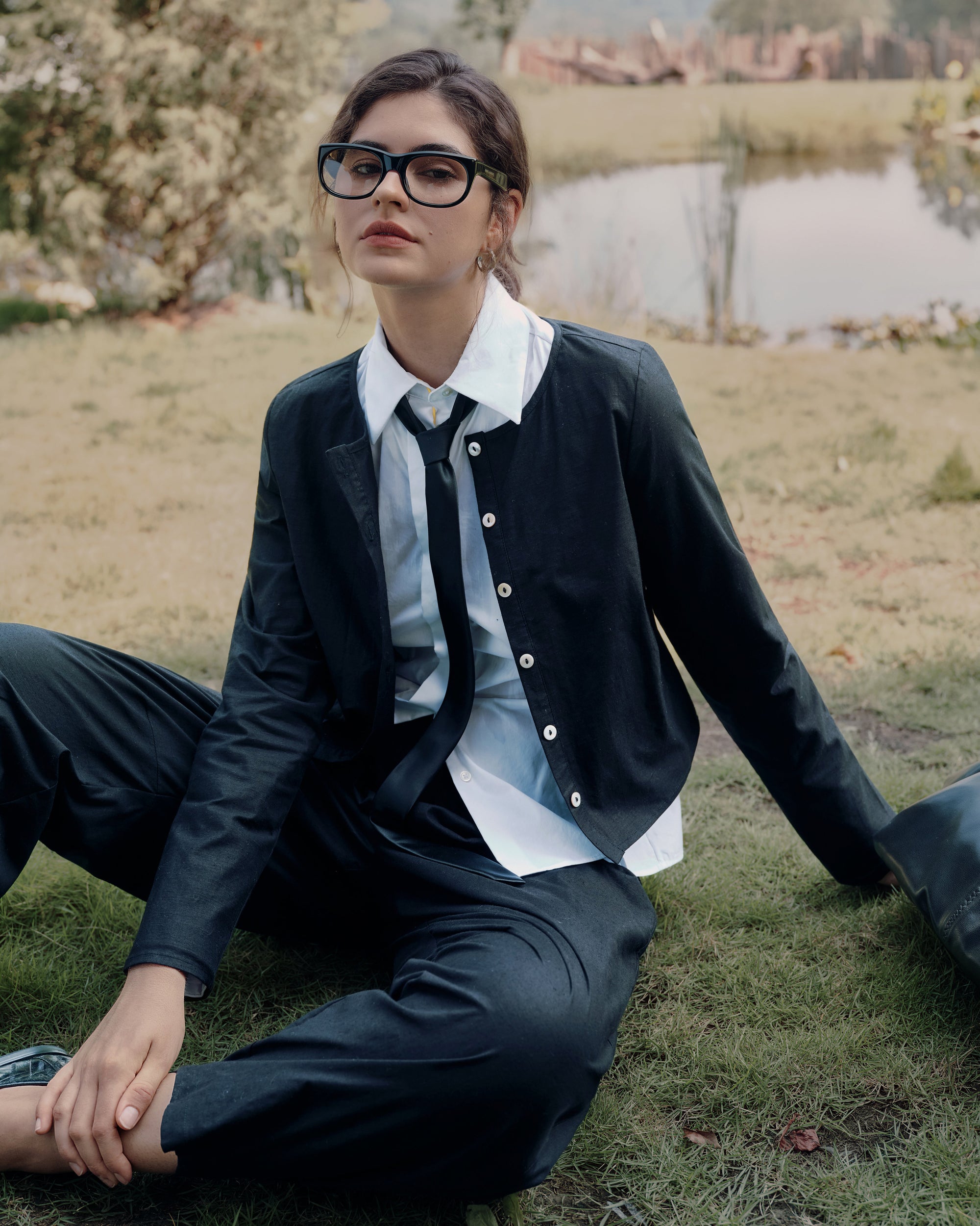 Side-profile on garden path of Aella Top black layered over white shirt with Aella Pants black; clean neckline and relaxed taper.