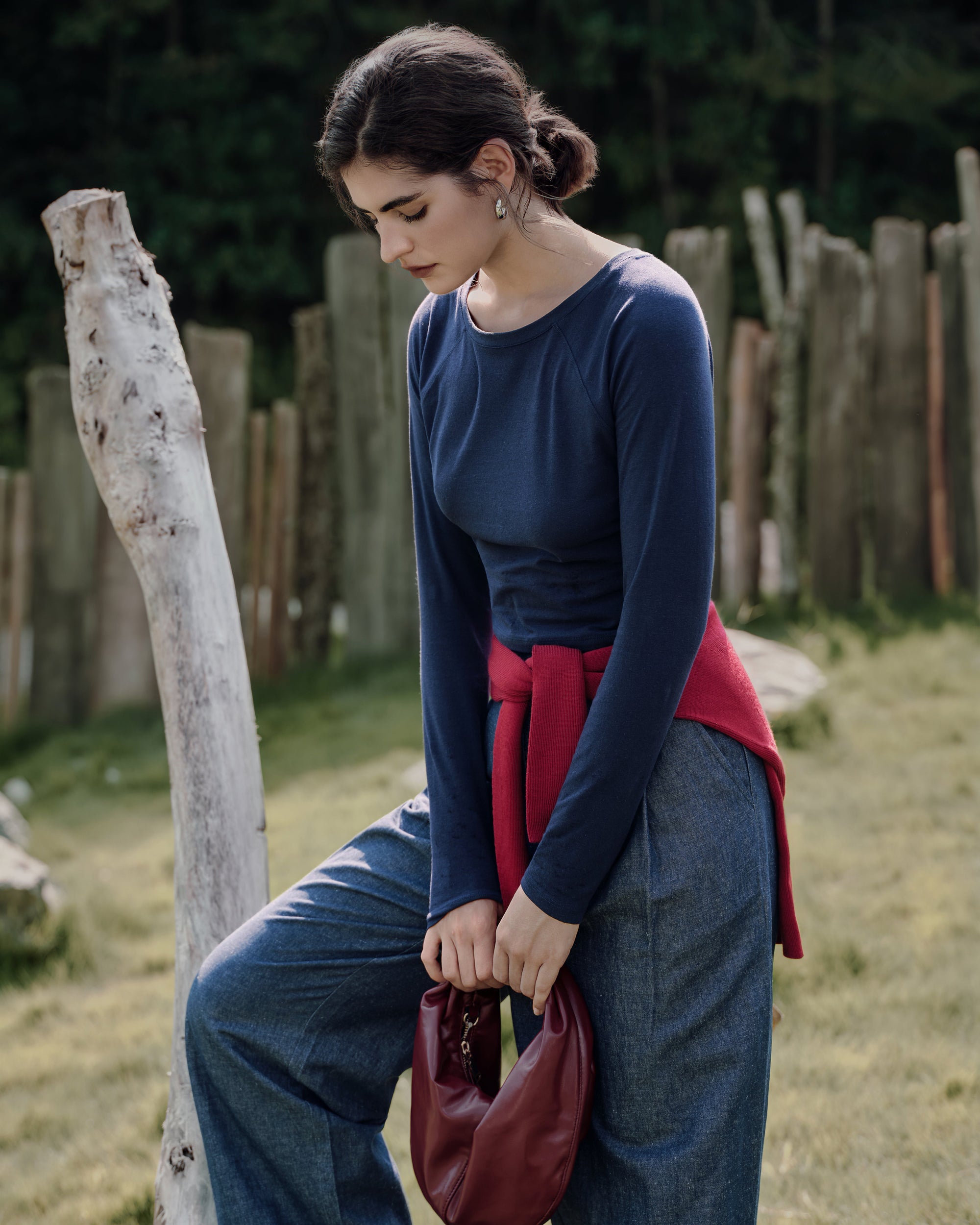 One foot on the log showing cropped hem of tee and elongating high rise trouser silhouette in indigo.