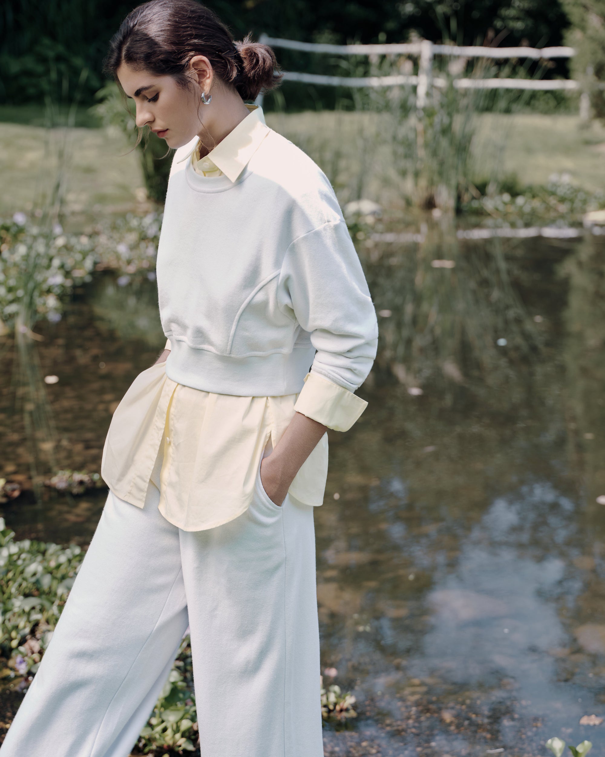 Three-quarter walk-away by the lake showing back view of the white fleece set over long light-yellow shirt; relaxed, seasonless layering.