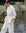 Three-quarter walk-away by the lake showing back view of the white fleece set over long light-yellow shirt; relaxed, seasonless layering.