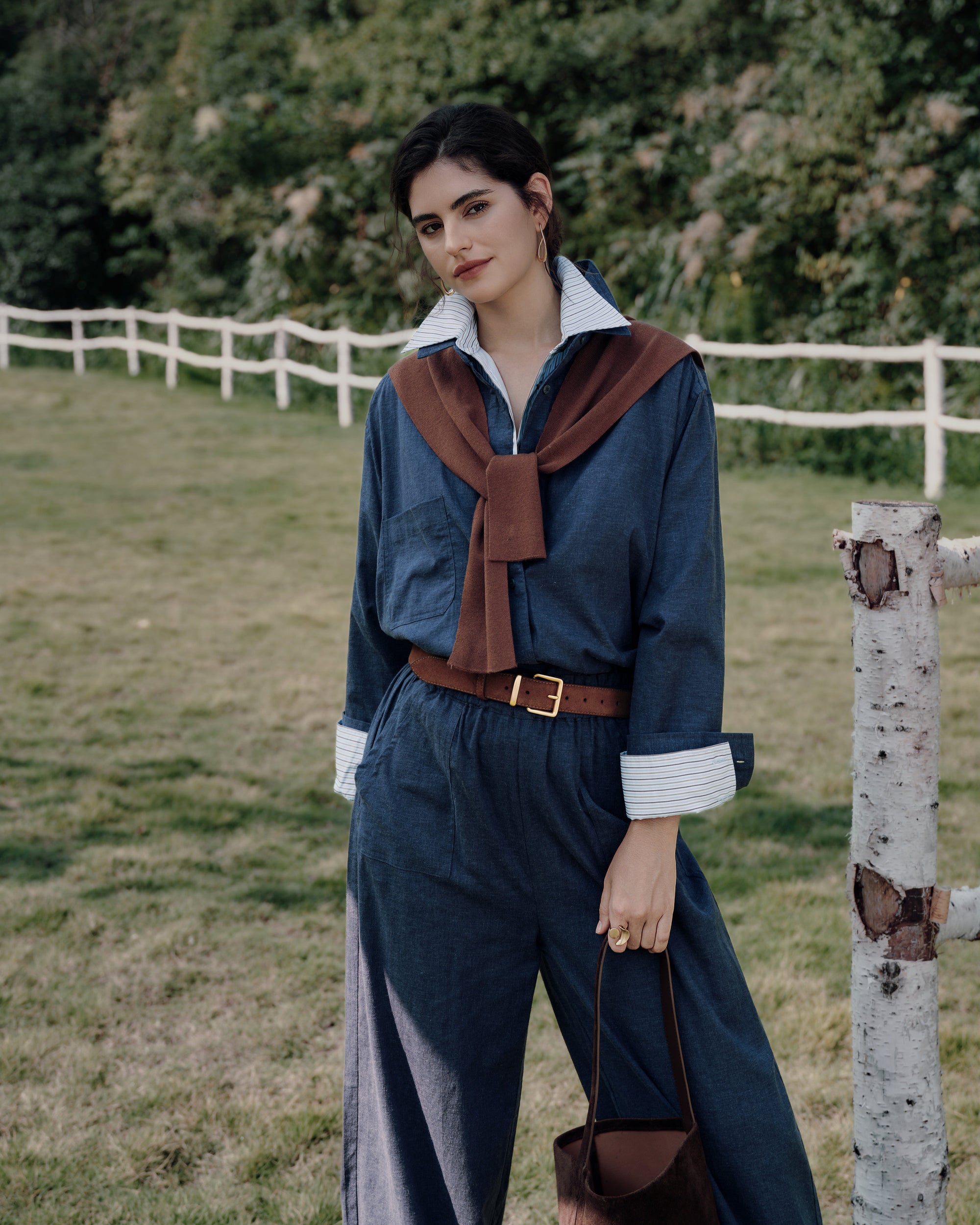 Standing next to a farmhouse fence wearing Lyricist set indigo blue over white shirt; relaxed fit and refined twill texture.