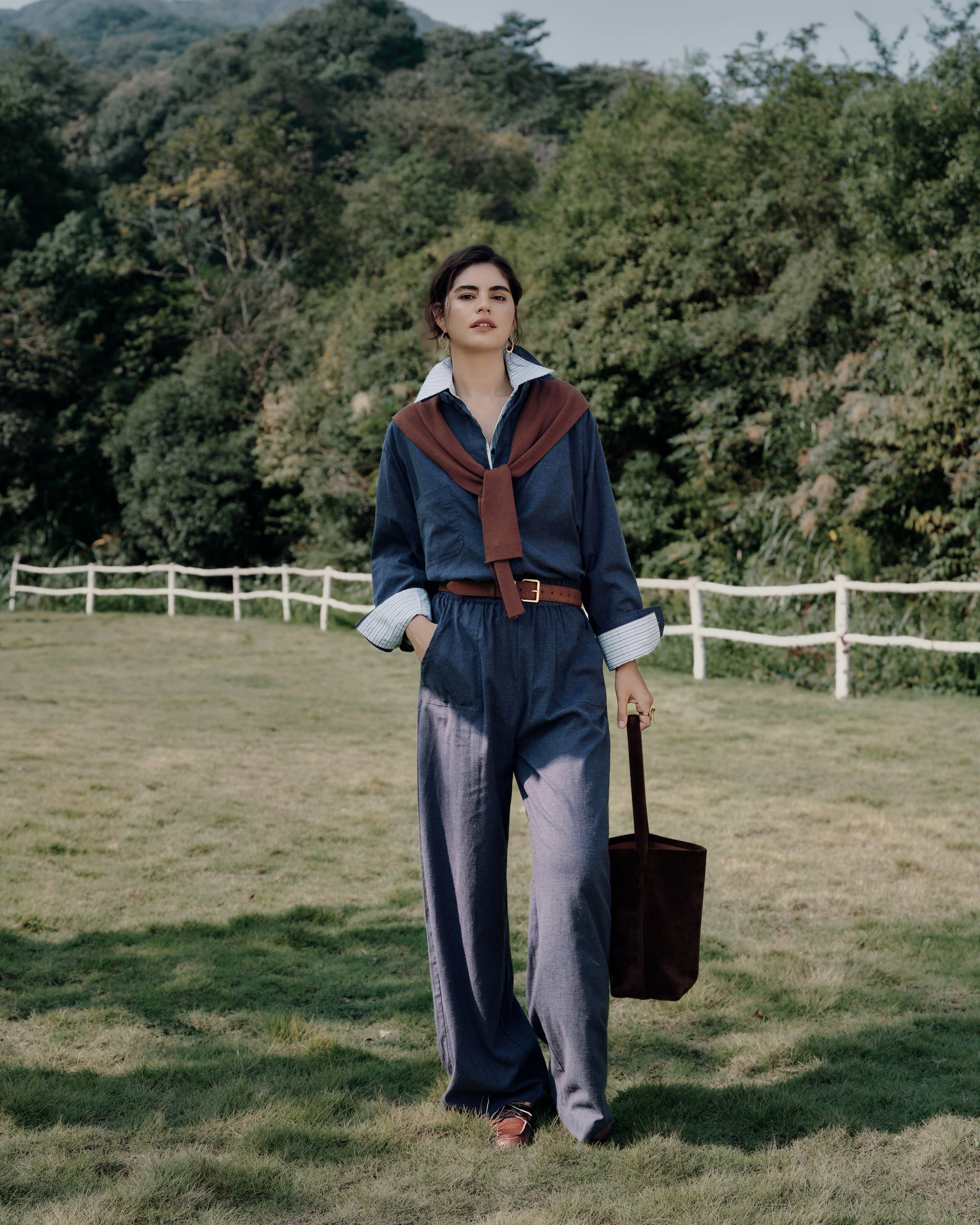 Backlit portrait near a white fence: Lyricist Shirt indigo blue layered over white shirt with matching Pull-on Pants indigo blue; soft twill sheen and relaxed drape.