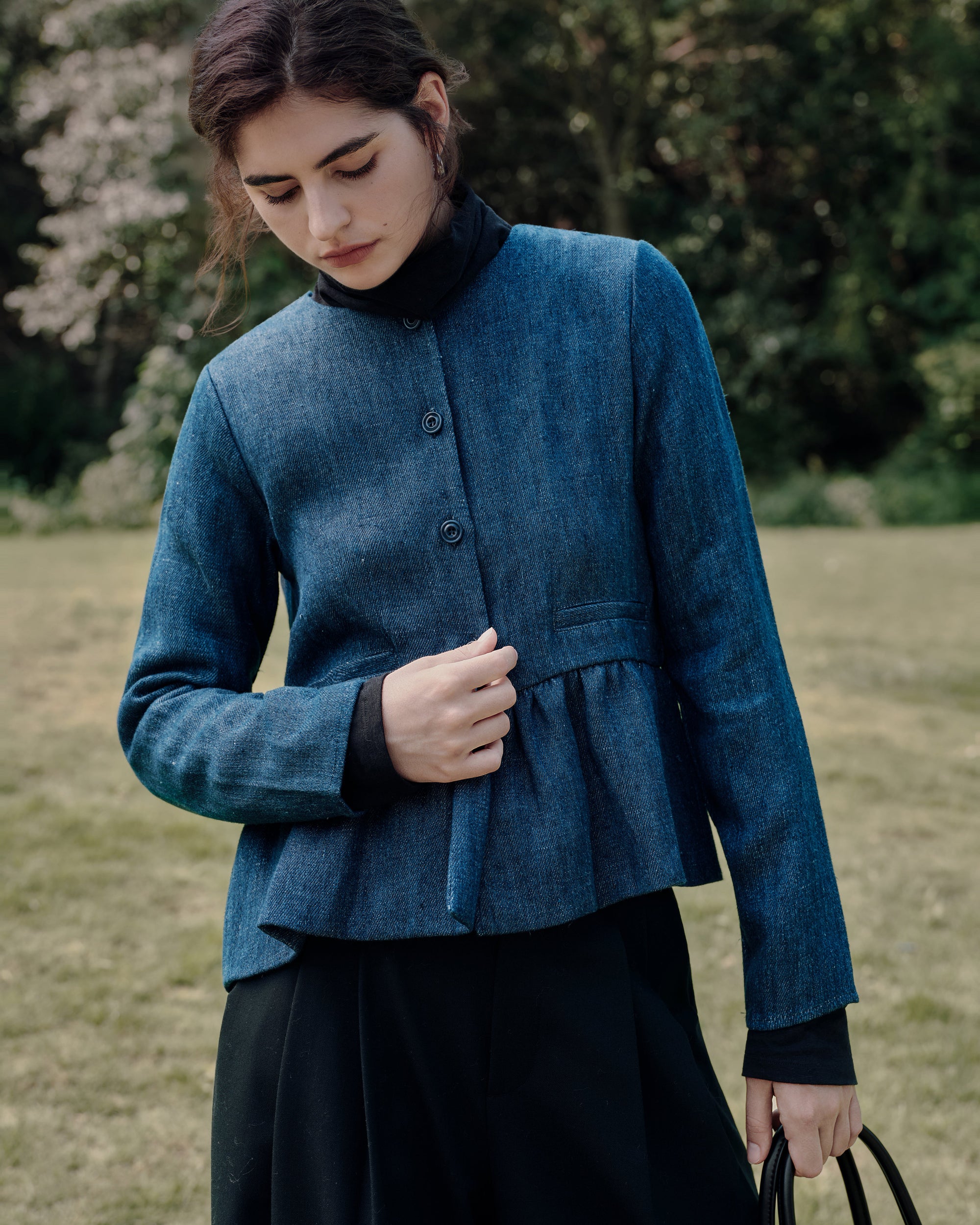 Model wearing Juana Denim Atelier Peplum Jacket (blue denim, pure hemp) layered over Ossa Knitted Hemp Turtleneck (black, merino–silk–hemp knit), styled for elevated everyday wear.