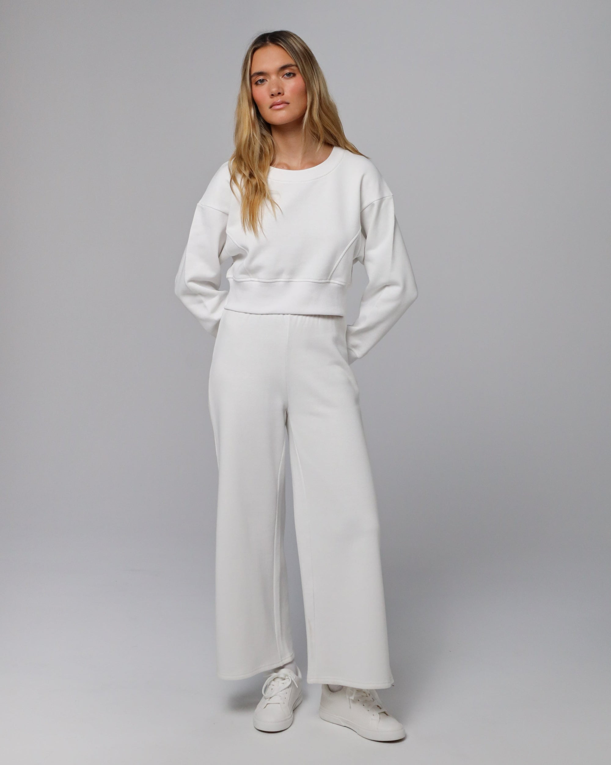 Model wearing coordinated white fleece set (cropped sweater + sweatpants); front view.