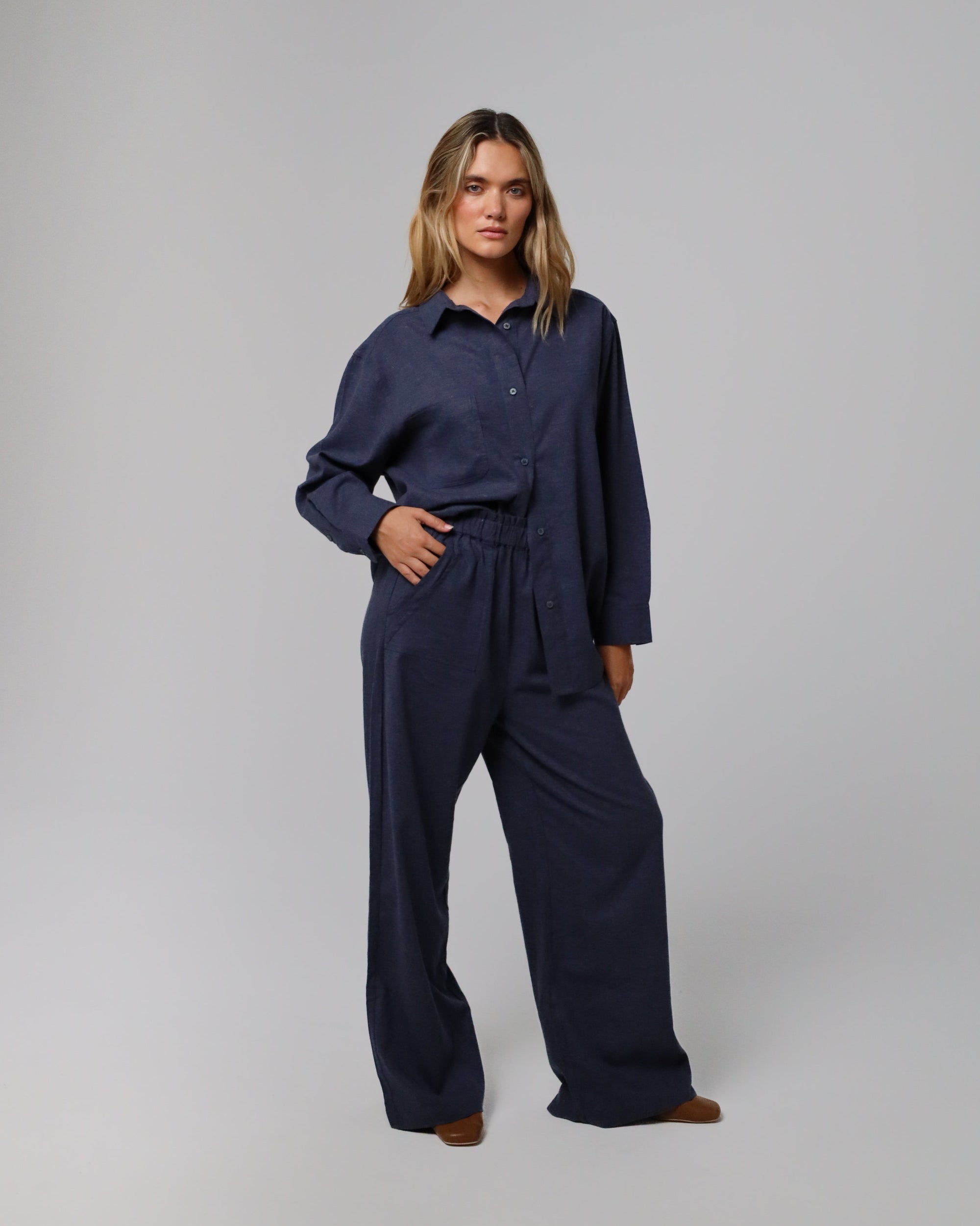 Woman wearing Juana Lyricist High Rise Pull-on Pants in an indigo blue hemp–Tencel™ twill blend, styled for sustainable everyday wear.