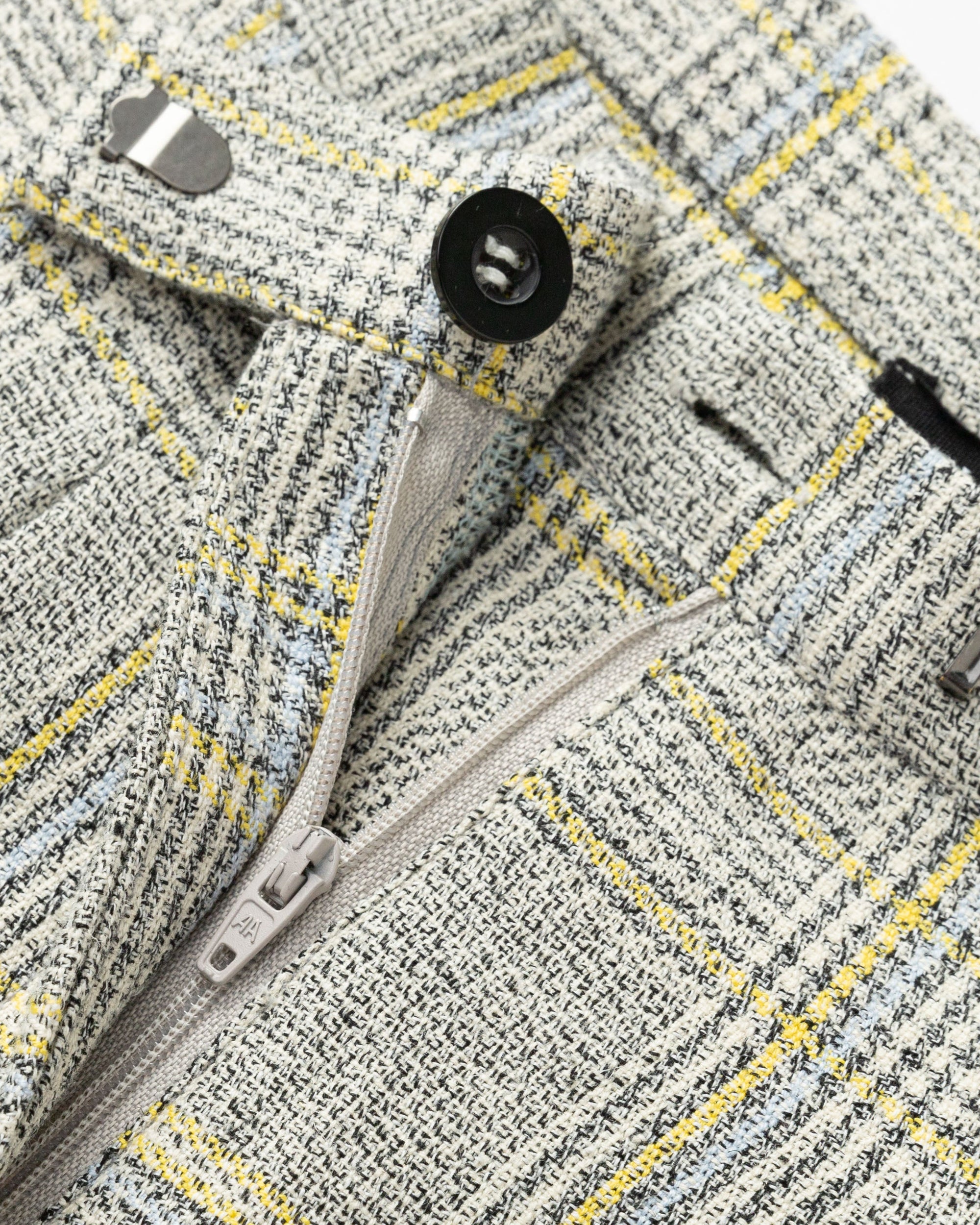 Flat lay of Plaid Theory High Rise Trousers (yellow-grey plaid), showing waistband, corozo button, and finishing.