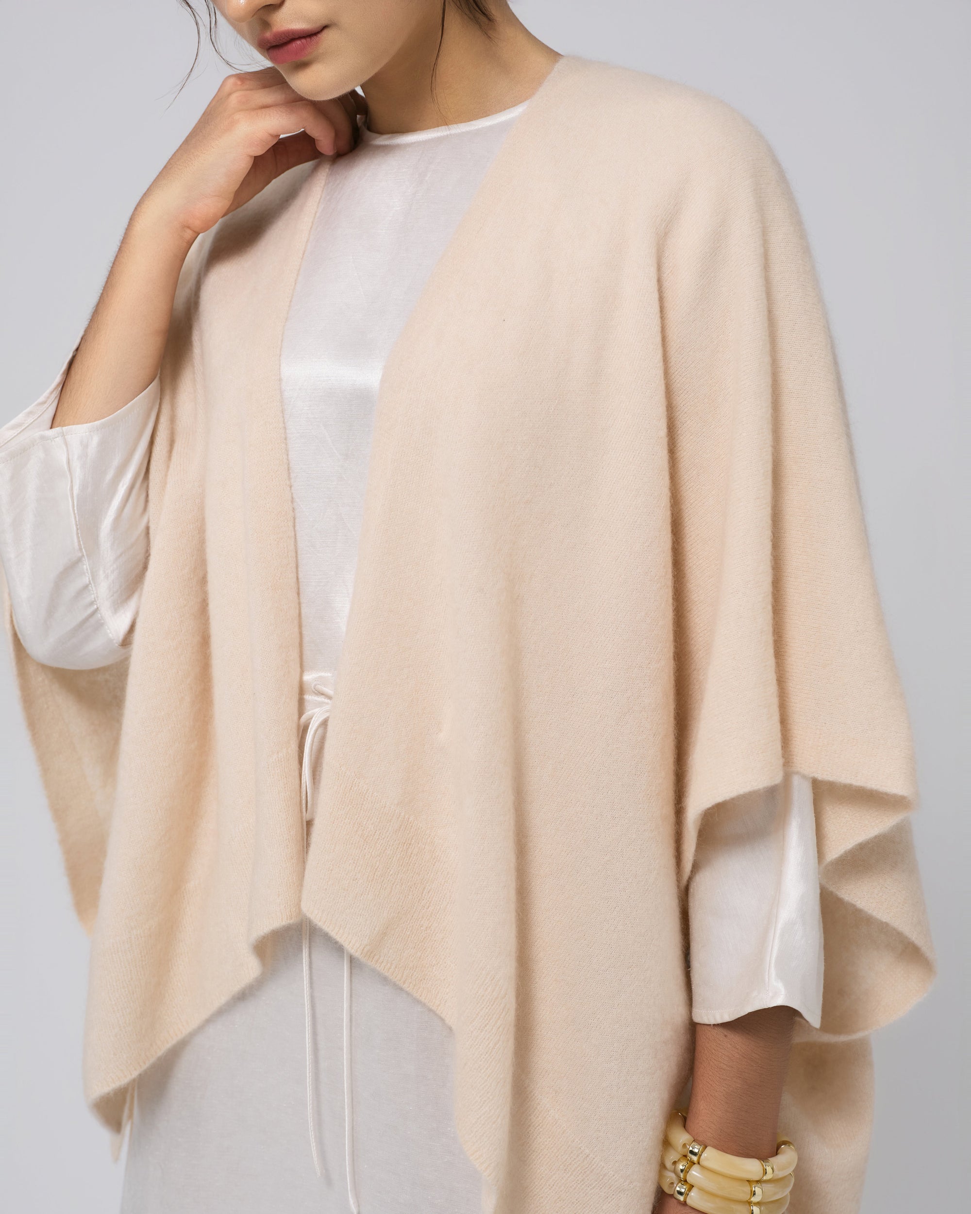 Model wearing Juana Cashmere Cape in almond milk (wool–cashmere–hemp knit), showing fluid drape and sculptural silhouette.